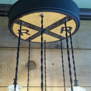 May include: A unique ceiling light fixture with a black metal frame and a yellow and black railroad crossing sign design. The fixture has multiple black twisted cords with clear glass light bulbs.