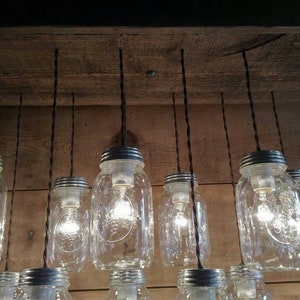 May include: A rustic wooden chandelier with multiple clear glass mason jars hanging from black cords. Each jar has a silver lid and contains a light bulb.