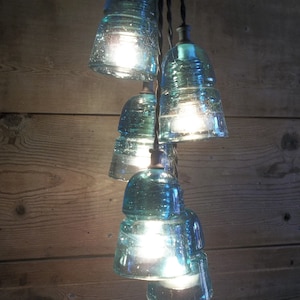 May include: A unique chandelier featuring five teal-colored glass insulator light fixtures. The lights hang from black cords against a wooden plank background. The text "BUNCHED Style" and "All wires coming from center hole" is visible.