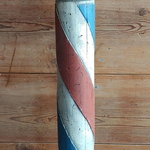May include: A vintage barber pole with a blue sphere on top, a red and white striped column, and a dark base. The pole is made of wood and has a distressed, aged appearance, suggesting it is an antique.