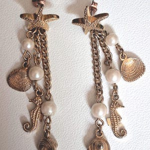 May include: Gold-toned earrings featuring starfish studs, chains, faux pearls, seahorse charms, and seashell pendants. These dangle earrings have a nautical theme, perfect for beach or ocean-themed outfits.