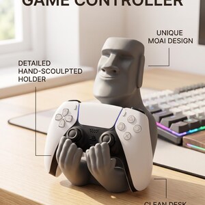 May include: A gray Moai-shaped holder designed to support a white and black game controller. The text GUARDIAN OF THE GAME CONTROLLER is displayed above the figure, with labels pointing to the detailed hand-sculpted holder and unique Moai design.
