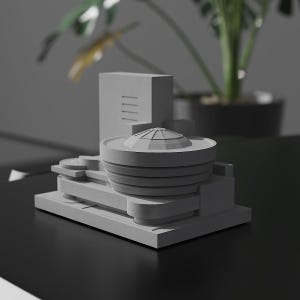 Könnte beinhalten: Graues Architekturmodell des Guggenheim Museums. Das Modell zeigt eine zylindrische Zentralstruktur mit gewölbtem Dach, umgeben von rechteckigen und gebogenen Elementen. Das Modell steht auf einer schwarzen Oberfläche mit einer Pflanze im Hintergrund.
