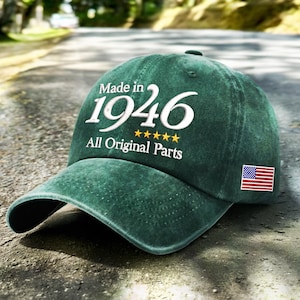 May include: A dark green baseball cap with a distressed finish. The front features white text that reads Made in 1946, followed by five yellow stars and the text All Original Parts. A small rectangular American flag patch is on the side.