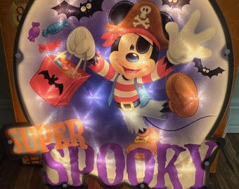 May include: A round Halloween decoration featuring a cartoon pirate mouse with a red and white striped shirt, pirate hat, and eye patch. The decoration includes the words "SUPER SPOOKY" and images of bats and candy.
