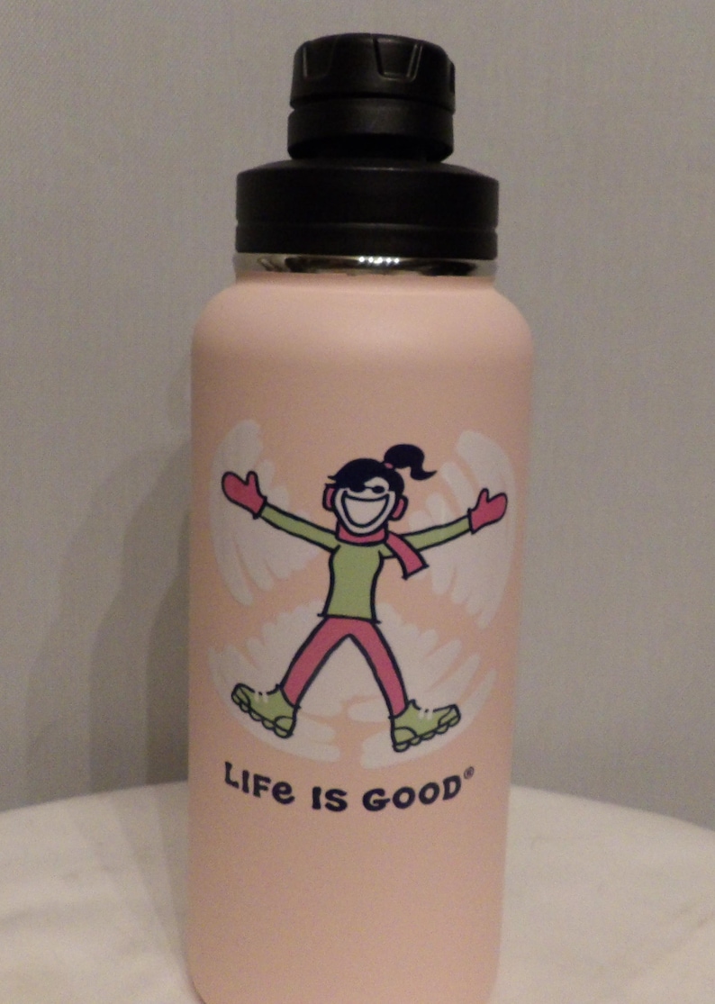 K&ouml;nnte beinhalten: Eine hellrosa isolierte Wasserflasche mit schwarzem Deckel. Die Flasche zeigt eine Grafik einer Person, die einen Schneeengel macht, mit gr&uuml;nem Hemd, rosa Hose und rotem Schal. Die Worte "Life is good" sind darunter gedruckt.
