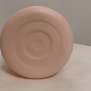 K&ouml;nnte beinhalten: Nahaufnahme des Bodens eines hellrosa, runden Objekts. Der Boden hat eine Reihe konzentrischer Kreise, die von der Mitte ausgehen. Das Objekt befindet sich vor einem neutralen Hintergrund.
