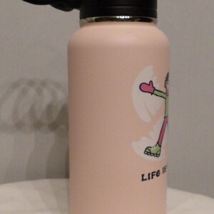 K&ouml;nnte beinhalten: Eine hellrosa isolierte Wasserflasche mit schwarzem Deckel und Griff. Die Flasche zeigt eine Cartoon-Grafik einer Person, die einen Schneeengel macht, mit den Worten "Life is" unter der Grafik.