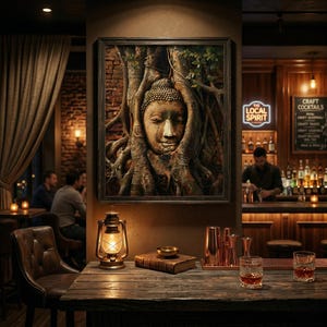 Op de afbeelding: Een ingelijst kunstwerk met een sereen Boeddha-gezicht verweven met boomwortels hangt in een zwak verlichte bar. De bar heeft een houten aanrecht, een vintage lantaarn en twee glazen amberkleurige vloeistof. Het bord luidt "The Local Spirit".