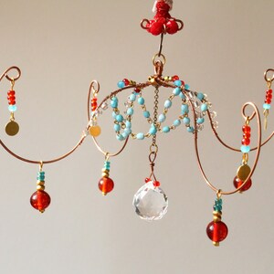 May include: A handcrafted copper wire chandelier with turquoise, red, and clear beads. The chandelier features a central crystal ball and decorative gold-coloured accents. The design is intricate and delicate, suitable for home decor.
