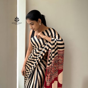 Könnte beinhalten: Ein schwarz-beige gestreifter Sari mit einem rot-beige gemusterten Rand. Der Sari ist über einer Person drapiert, die ein schwarzes Oberteil trägt. Das Logo von Ethnic Craft India ist oben links sichtbar.