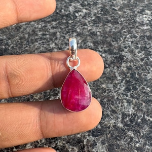 Puede incluir: Un colgante de rubí facetado en forma de lágrima con una fianza de plata. La vibrante gema roja está engastada en un bisel de plata, creando un contraste llamativo. El colgante está diseñado para ser usado como collar.
