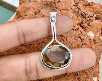 May include: A silver pendant with an oval, smoky quartz gemstone. The pendant has a simple, elegant design with a loop at the top for a chain. The gemstone is a warm brown color and is set in a silver bezel.