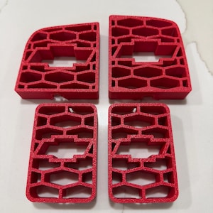 May include: Four red, geometric car emblem inserts. Each piece features a honeycomb pattern and the Chevrolet logo. The pieces are arranged in a square, showcasing the design and color.