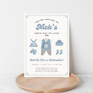 Peut inclure: Carte d'invitation bleu clair et blanche avec le texte "Vous êtes invité à la 100e journée de Nick !" et des illustrations de vêtements coréens traditionnels. La carte est sur un plateau en bois.