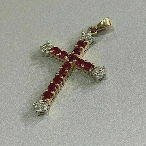 May include: A gold-toned cross pendant adorned with vibrant red gemstones and sparkling white diamonds. The cross features a classic design with a loop for a chain. The gemstones are set in a row, creating a striking contrast against the gold.