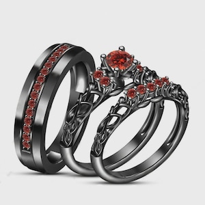 May include: A set of black wedding rings. The rings feature red gemstones. One ring has a row of small gems, while the other two have a floral design with a large center gem and smaller gems. The rings are set against a white background.