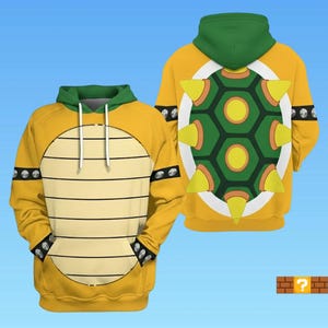 May include: Yellow hoodie with a green hood and a shell design. The front features a shell pattern, while the back showcases a green and yellow shell design. The sleeves have black accents with silver studs. A fun, themed sweatshirt.