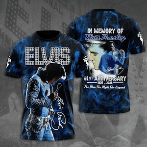 May include: Two blue and black t-shirts featuring Elvis Presley. One has "ELVIS" in white block letters and an image of Elvis. The other says "IN MEMORY OF Elvis Presley" and "91 ST ANNIVERSARY".