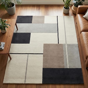 Peut inclure: Un tapis rectangulaire avec un motif géométrique. Le tapis présente de grands blocs de couleurs dans les tons de noir, beige, gris et marron. De fines lignes grises et noires définissent les formes. Le tapis est posé sur un parquet.
