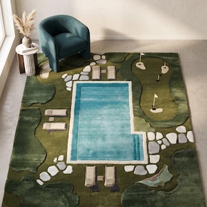 May include: A rectangular area rug featuring a top-down landscape design. The rug displays a central rectangular turquoise swimming pool, surrounded by green grass, light-coloured stone pathways, lounge chairs, and a putting green with flags.