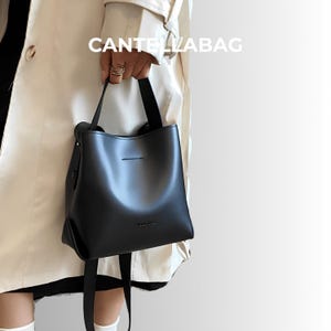 May include: A black handbag with short handles is held. The bag has a structured shape and a smooth surface. The text "CANTELABAG" is visible in white letters above the bag.