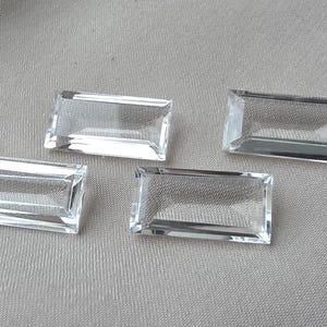 Op de afbeelding: Vier heldere, rechthoekige edelstenen met facetranden worden getoond op een grijze ondergrond. De edelstenen zijn transparant, laten licht door en hebben een gepolijste uitstraling. De edelstenen zijn waarschijnlijk voor het maken van sieraden.