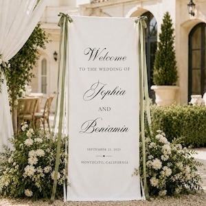 May include: A tall, rectangular white fabric wedding welcome sign featuring black serif and script text that reads Welcome to the wedding of Sophia and Benjamin, September 21, 2025, Montecito, California, accented by olive green ribbons.