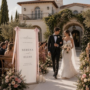 May include: A tall rectangular wedding welcome sign with a gold frame and pink ribbons, displaying the text Welcome to the wedding of Serena and Elias, August 14, 2025, Highclere Castle, positioned next to a couple walking down an aisle.