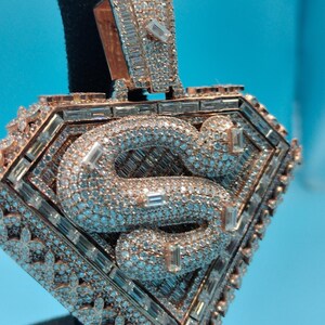 May include: A diamond-encrusted pendant with a rose gold finish. The pendant features a diamond-studded snake design within a diamond-shaped frame. The frame is also adorned with diamonds, creating a luxurious and eye-catching piece of jewelry.