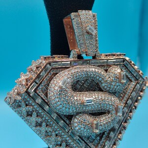 May include: Rose gold pendant with a diamond-encrusted 'S' design. The pendant is shaped like a diamond and features a floral pattern around the edges. The bail is also encrusted with diamonds.