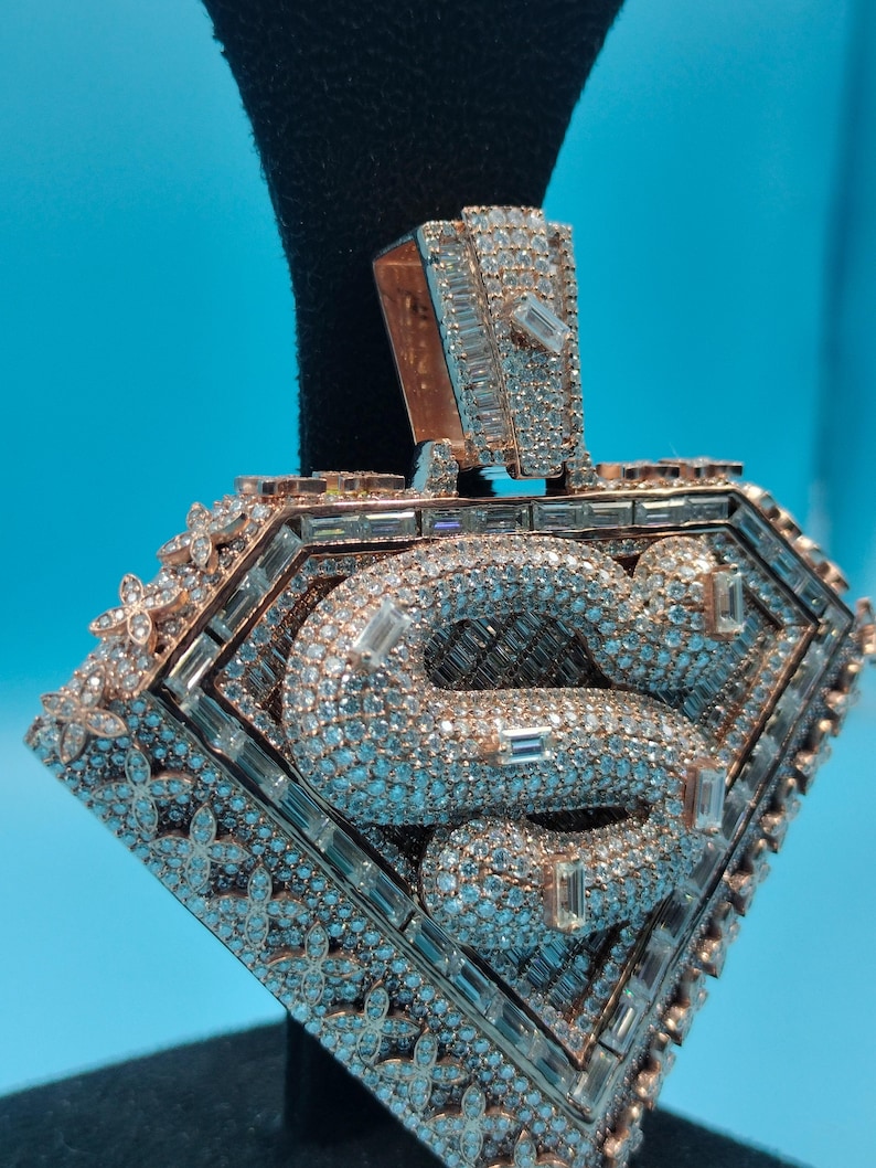 May include: Rose gold pendant with a diamond-encrusted 'S' design. The pendant is shaped like a diamond and features a floral pattern around the edges. The bail is also encrusted with diamonds.