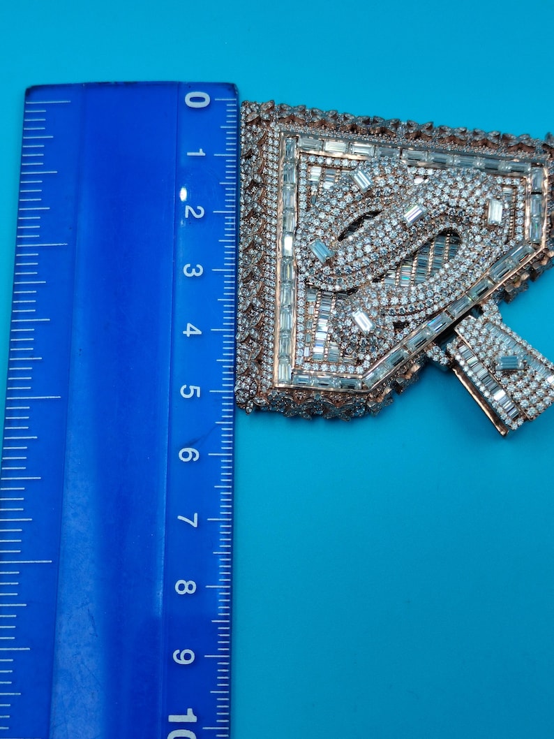 May include: An ornate, jeweled applique with a geometric design, featuring clear and silver-toned crystals. The applique is approximately 4 inches long, with a copper-colored border, set against a blue background.