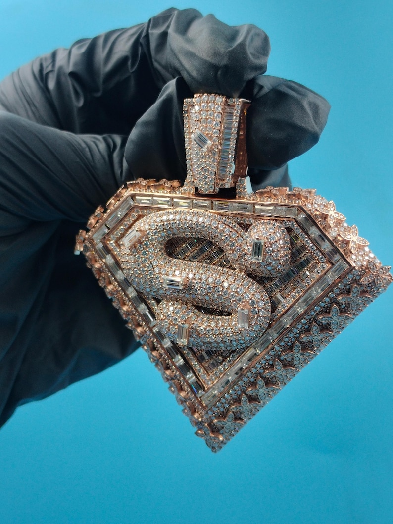 May include: A diamond-encrusted pendant in a rose gold setting. The pendant features a snake design within a diamond-shaped frame, with intricate detailing and sparkling stones. The background is a solid blue.