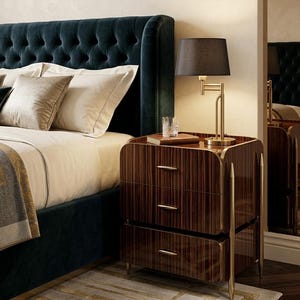 May include: A dark wood nightstand with three drawers, gold-toned metal accents, and a matching gold-toned table lamp with a black shade. The nightstand features a vertical striped wood grain pattern and sits beside a tufted dark teal bed.