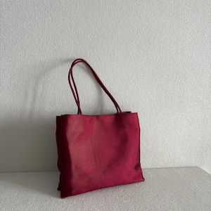 Peut inclure: Un sac fourre-tout rectangulaire rouge fonc&eacute; fabriqu&eacute; dans un tissu lisse semblable &agrave; du satin. Le sac pr&eacute;sente deux fines bretelles assorties fix&eacute;es au bord sup&eacute;rieur, offrant une silhouette simple et structur&eacute;e avec un l&eacute;ger &eacute;clat.