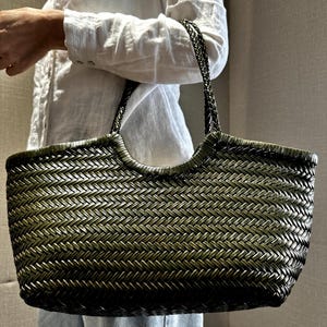 Peut inclure: Un sac fourre-tout tissé vert olive et noir. Le sac a une forme rectangulaire avec une ouverture de poignée incurvée et des poignées tressées. Le motif de tissage crée une surface texturée.