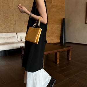 Peut inclure: Une robe noire sans manches arrivant au genou port&eacute;e sur une jupe blanche &eacute;vas&eacute;e. La tenue est accessoiris&eacute;e avec un sac &agrave; main rectangulaire en m&eacute;tal dor&eacute; dot&eacute; de deux fines anses et un bracelet argent&eacute; au poignet.
