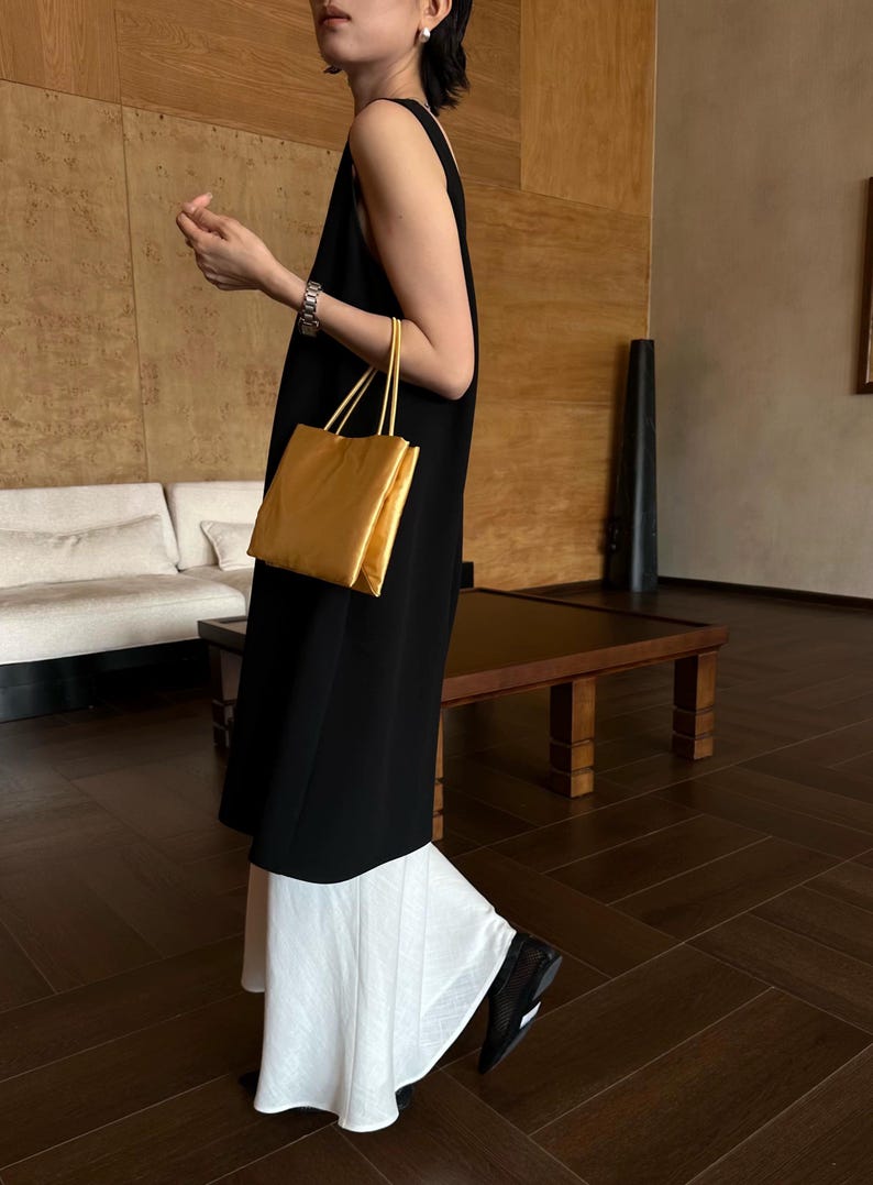 Peut inclure: Une robe noire sans manches arrivant au genou port&eacute;e sur une jupe blanche &eacute;vas&eacute;e. La tenue est accessoiris&eacute;e avec un sac &agrave; main rectangulaire en m&eacute;tal dor&eacute; dot&eacute; de deux fines anses et un bracelet argent&eacute; au poignet.