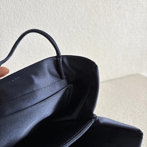 Peut inclure: Un sac &agrave; main en satin bleu marine fonc&eacute; dot&eacute; d'une finition lisse et lustr&eacute;e, d'une fine poign&eacute;e sup&eacute;rieure unique et d'une ouverture structur&eacute;e. L'int&eacute;rieur est doubl&eacute; d'un tissu bleu marine assorti avec des coutures nettes sur les bords.
