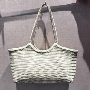 以下が含まれることがあります： 編み込まれた白いトートバッグ、編み込みのハンドル付き。 バッグは長方形で、上端がカーブしており、織り模様があります。 ハンドルは、金属リングでバッグの上部に固定されています。