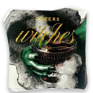 May include: A stack of black and green paper napkins with gold foil lettering that reads "Cheers Witches". The napkins feature a watercolor illustration of a hand holding a goblet.