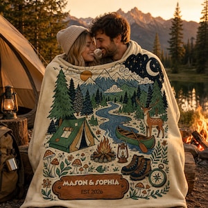 May include: A cream-coloured throw blanket featuring a colourful outdoor scene with a green tent, a river, a deer, a canoe, a campfire, and hiking boots. The design includes the text MASON & SOPHIA and EST. 2026 printed on a wooden-style sign graphic.