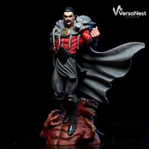Puede incluir: Figura detallada de un personaje con un atuendo rojo y negro, con una capa gris y un cuello de piel de lobo. La figura se encuentra sobre una base roja con forma de monstruo. La figura tiene bigote y hace un gesto con la mano.