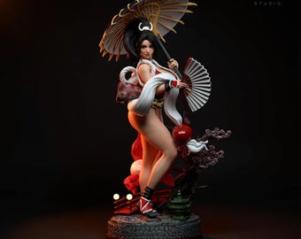 May include: A detailed figurine of a woman in a traditional Japanese outfit, holding a parasol and a fan. The figure is predominantly red and white, with black hair and accents. The base is a stone-like texture, and the studio logo is visible.