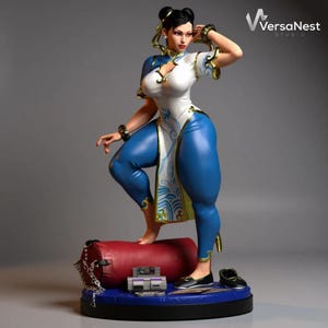 May include: A detailed figurine of a female character in a white and blue outfit, posed on a red cylinder. The figure is standing on a blue base with a video game console and black shoes. The figure has black hair and gold accents.
