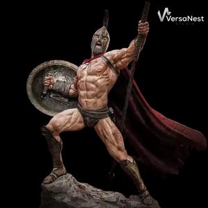 Può includere: Statua dettagliata di un guerriero spartano in battaglia. La figura è muscolosa, indossa un elmo, uno scudo e un'armatura, e tiene una lancia e una spada. Un mantello rosso fluttua dietro di lui. La statua è su una base rocciosa.