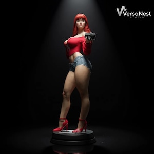 Könnte beinhalten: Eine Statue einer Frau mit roten Haaren, die ein rotes Oberteil, Jeansshorts und rote High Heels trägt und eine Kamera hält. Die Statue steht auf einem schwarzen Sockel vor dunklem Hintergrund. Das Logo von VersaNest Studio befindet sich oben rechts.