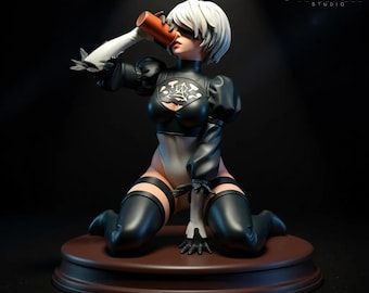 May include: A detailed figurine of a female character in a black and white outfit, kneeling and drinking from a brown cylinder. The figure has short white hair and is on a brown base. The logo "VersaNest STUDIO" is in the top right.