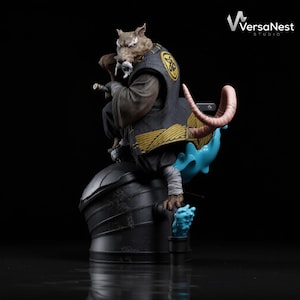 May include: A detailed figurine of a rat-like character in a black and gold outfit, holding a sword. The figure is seated on a dark, textured base with blue and pink accents. The VersaNest Studio logo is visible in the top right corner.